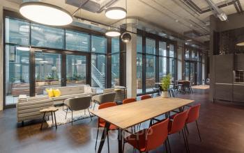 Modern office space rental at Hussitenstraße 32, Berlin Mitte, featuring open seating with red chairs, wooden tables, and a relaxed lounge area with grey sofas.