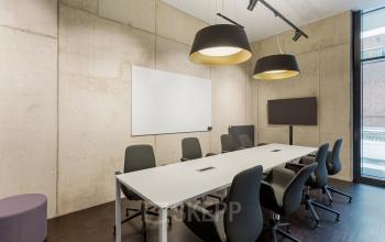 Modern conference room with concrete walls, equipped with a large table, chairs, screen, and video conference facilities in Berlin Mitte at Hussitenstraße 32.
