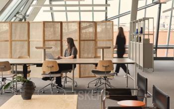 Büro in Karl-Liebknecht-Straße 29a, Berlin Mitte, mit großen Fenstern. Eine Person arbeitet am Laptop und eine andere geht im Hintergrund.