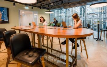 Moderner Büroraum mieten in Berlin Mitte, Linkstraße 2, mit großen Tischen, bequemen Stühlen und Personen bei der Arbeit an Laptops.