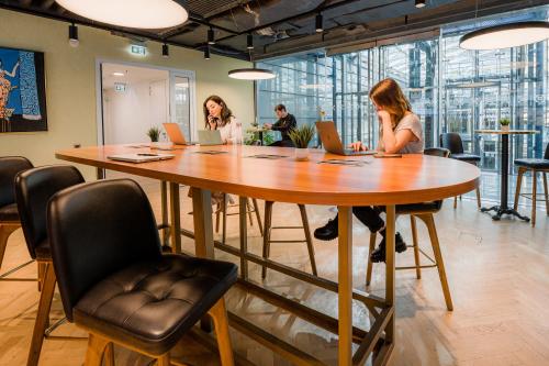 Moderner Büroraum mieten in Berlin Mitte, Linkstraße 2, mit großen Tischen, bequemen Stühlen und Personen bei der Arbeit an Laptops.
