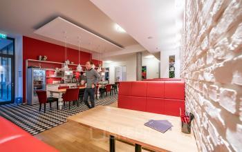 Moderne Bürofläche in Berlin Mitte, Unter den Linden 10, mit stilvollen roten und weißen Möbeln, einer gemütlichen Atmosphäre und einer Person, die durch den Raum geht.