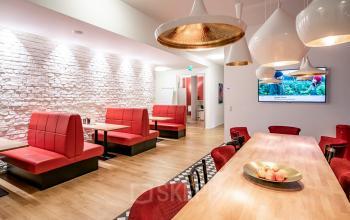 Moderner Büroraum in Berlin Mitte mit roten Sitzbänken und Holztischen, ideal zum Büromieten. Stilvoll erleuchtet mit Pendelleuchten.