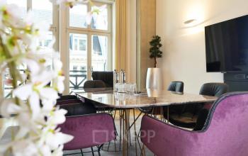 Moderner Konferenzraum in Berlin Mitte, Unter den Linden 10, mit stilvollen lila Stühlen und großem Bildschirm. Perfekte Umgebung für Meetings und Präsentationen. Ideal, um einen Büroraum zu mieten.