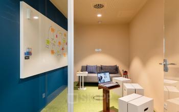 Moderner Büroraum am EUREF-Campus 22 in Berlin Schöneberg mit einem Whiteboard, einem kleinen Tisch und einer Couch. Ideal für kreatives Arbeiten und Meetings. Perfekt zum Büro mieten.