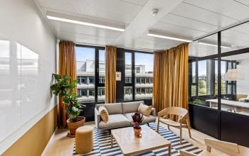 Moderner Büroraum in der Weltpoststrasse 5 in Bern mit großem Fenster, gemütlicher Sitzecke und Pflanzen, ideal zum Büro mieten.