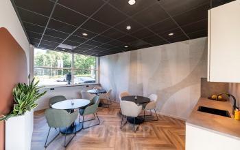 Modern office space at De Maas 8, Best, featuring stylish furnishings with round tables and chairs, large window providing natural light, and sleek wooden flooring, ideal for office space rental.