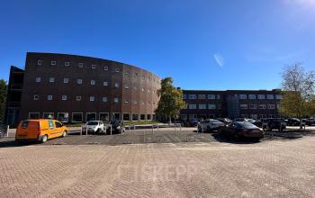 Exterior view of an office building located at De Maas 8 in Best, showcasing a modern design with ample parking space in front.