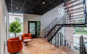 Modern stairwell at De Maas 8 in Best, featuring a sleek interior with wooden flooring and vibrant orange seating.