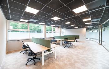 Modern office space with multiple workstations and green partitions, featuring large windows allowing ample natural light, located at De Maas 8, Best. Ideal for office space rental with comfortable seating.