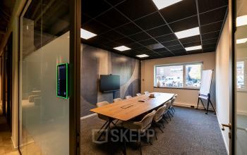 Conference room at De Maas 8, Best, featuring a long table, chairs, a wall-mounted screen, and ample natural light. Ideal office space rental for meetings and collaborative sessions.