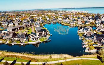 A scenic aerial view of a lake surrounded by modern residential houses in Blaricum, with green spaces providing a tranquil environment.