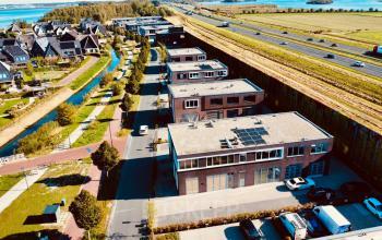 Exterior view of Deltazijde 20b, Blaricum, featuring an office building with surrounding green landscape and nearby highway, positioned in a peaceful business area ideal for office space rental.