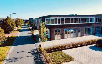 Exterior view of a modern office building at Deltazijde 20b, Blaricum, featuring large glass windows and a well-maintained surrounding area. Ideal for those seeking office space rental in a professional environment.