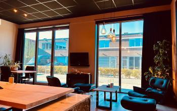 Bright and welcoming office to rent at Deltazijde 20b, Blaricum, featuring modern furnishings, ample natural light from large windows, and stylish lighting fixtures in a spacious lounge area.