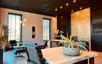 Spacious and modern office interior at Deltazijde 20b, Blaricum, featuring stylish wooden tables and leather chairs, perfect for office space rental. Warm lighting and large windows create a welcoming atmosphere.