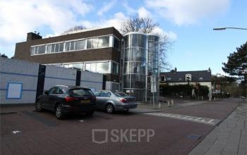 Exterior view of office building at Zomerzorgerlaan 50, Bloemendaal, showing modern architecture with a glass cylindrical elevator and parking space.