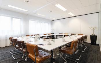 Modern conference room at Tolnasingel 1 - 3, Bodegraven with large windows, white tables, brown chairs, and minimalistic decor. Ideal office space rental location.