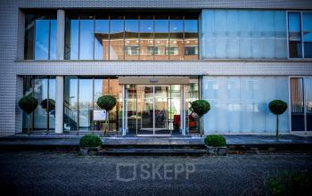 Exterior view of the office building at Tolnasingel 1 - 3, Bodegraven, featuring floor-to-ceiling windows and trimmed greenery at the entrance, highlighting the office space rental opportunities.