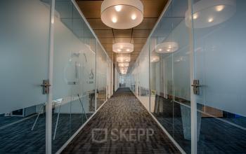 Modern hallway with glass office doors at Tolnasingel 1-3, Bodegraven, ideal for office space rental, featuring contemporary lighting and carpeted flooring.