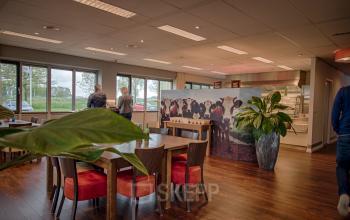 Spacious office lounge at Tolnasingel 1 - 3, Bodegraven with large windows, cozy seating area, and natural decor. Suitable for office space rental to enhance productivity.