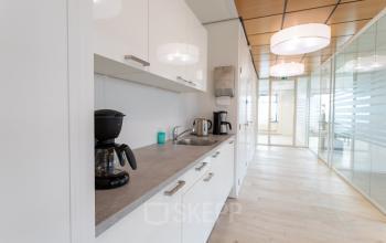 Modern pantry area in an office building with white cabinets, coffee makers, and stainless steel appliances at Tolnasingel 1 - 3, Bodegraven.