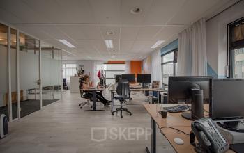 Modern office space at Tolnasingel 1 - 3, Bodegraven, featuring several workstations with computers and chairs, large windows providing natural light, and frosted glass walls.