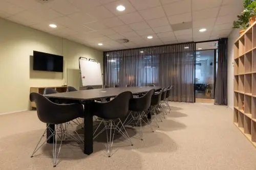 Spacious conference room with a long table and chairs, TV, whiteboard, and shelving, ideal for office space rental at Marktstraat 1-7, Bodegraven.