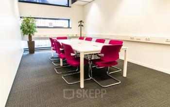Bright office space rental at Ceresstraat 1, Breda Centrum-Station, featuring a table with vibrant pink chairs and a potted plant.