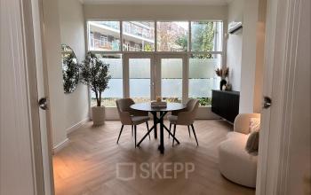 Bright office space with a round table and chairs, ideal for rent. Located in a peaceful setting with a view of the outside area through large windows.