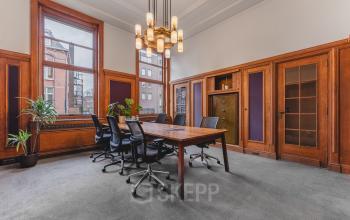 Office space for rent at Ceresstraat 13, Breda Centrum-Station, featuring a furnished meeting room with a large wooden table and chairs, surrounded by wooden paneling and large windows.