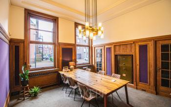 Stylish office space rental at Ceresstraat 13, Breda Centrum-Station featuring a large wooden table, vintage chandelier, and tall windows.