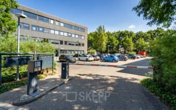Exterior view of the Westboek 36-66 office building in Breda Noord-West, featuring a parking area with multiple cars and lush greenery. Ideal for those seeking office space rental in a vibrant business district.