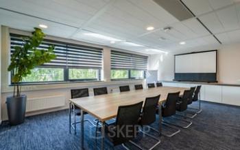 Spacious conference room with a large table and black office chairs, ideal for office space rental in Westboek 36-66, Breda Noord-West. Features include modern lighting and a projector for presentations.