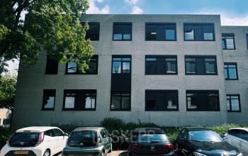 Exterior view of a modern office building at Druivenstraat 25-31 in Breda Oost, suitable for office space rental, with cars parked in front, framed by trees.