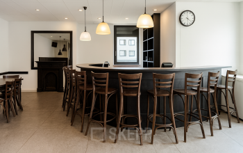 Elegant office space rental with a central bar-style table and wooden chairs, located at Druivenstraat 25-31, Breda Oost. Ideal for meetings or social gatherings.