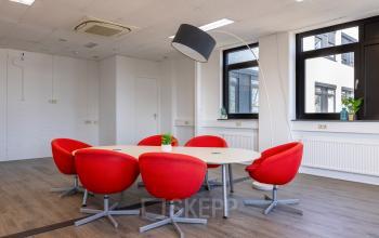 Office space with a round table surrounded by red chairs, featuring bright windows at Druivenstraat 25-31, perfect for meetings. Ideal office space rental in Breda Oost.