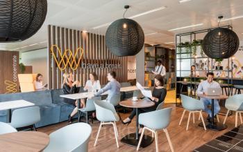 Office lounge area at Leonardo Da Vincilaan 1, Brussels Airport, Brussels, with people working on laptops, discussing at tables, and a modern interior design suitable for office space rental.