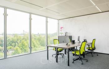 Bright office space to rent at Leonardo Da Vincilaan 1, Brussels Airport, featuring large windows, modern furniture, and vibrant green chairs.
