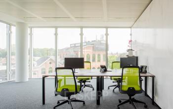Modern office space rental at Leonardo Da Vincilaan 1, Brussels Airport with large windows, natural light, and green chairs around white desks.