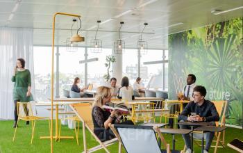 Bright and modern lounge area in the office space rental at Leonardo Da Vincilaan 1, Brussels Airport, with natural light, green decor, and people engaged in work-related conversations.
