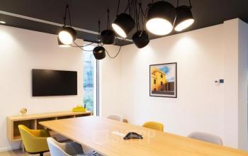 Modern furnished office to rent at Pegasuslaan 5, featuring a sleek meeting area with a large wooden table and stylish lighting, ideal for office space rental in Brussels Airport.