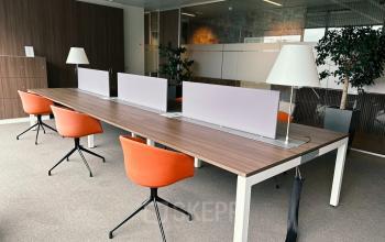 Modern office space with long wooden desk, orange chairs, partition dividers, and white lamps at Leonardo Da Vincilaan 19, Brussels Airport, ideal for office space rental.