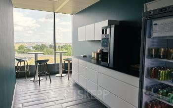 Modern pantry at Leonardo Da Vincilaan 19, Brussels Airport, featuring a coffee machine, tables, and chairs with a view of the runway.