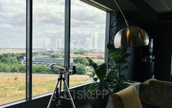 Bright office space rental at Leonardo Da Vincilaan 19, Brussels Airport, featuring a telescope and large windows overlooking a scenic view.
