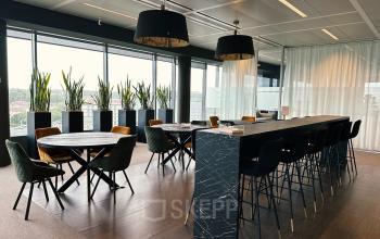 Modern furnished office space with large windows, plants, tables, and high seating at Leonardo Da Vincilaan 19, Brussels Airport, available for office space rental.