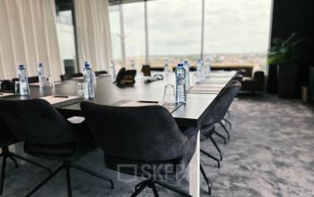 Modern conference room at Leonardo Da Vincilaan 19, Brussels Airport, featuring a large table, chairs, bottled water, and city views, suitable for office space rental.
