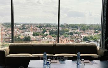 Office space for rent at Leonardo Da Vincilaan 19, Brussels Airport, featuring a large meeting table with water bottles and notebooks, overlooking a scenic city view through floor-to-ceiling windows.
