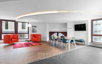 Modern office with colorful chairs around a large table, two orange armchairs, and a mounted TV at Koloniënstraat / Rue des Colonies 11 in Brussels Center, available for office space rental.