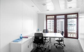 Office space rental at Koloniënstraat / Rue des Colonies 11, Brussels Center, featuring a bright room with modern white furnishings, several chairs around tables, and large windows overlooking city buildings.